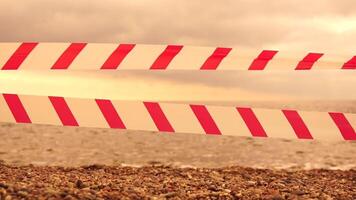 Red white warning tape barrier ribbon swinging in the wind across exotic sea beach background without people. No entry Red White caution tape. No holiday concept, delayed travel, no summer plans video