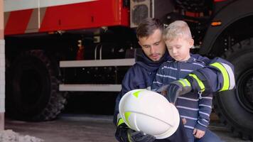 Happy little boy with firefighter in protective uniform in fire station video