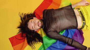 Gay man klädd i maska t-shirt lögner på gul bakgrund med en regnbåge flagga. begrepp mångfald, transsexuell, och frihet video