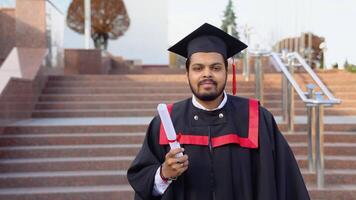 A young indian male graduate with diploma against the background of university video