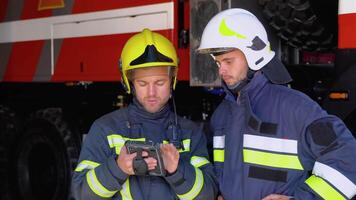 Two firemen in full equipped clothes standing outside at the fire truck with a tablet in hands and deciding what to do for extinguishing fire video