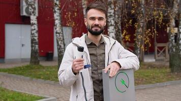 A bearded man with a charger at a charging station looks into the camera video