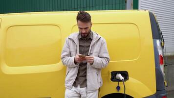 Young man smokes an electronic cigarette while electric car is charging on outdoor station video