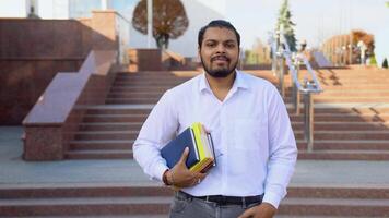 sonriente indio masculino estudiante con libros cerca Universidad video