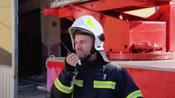 Brave firefighter man talking to walkie talkie with fire truck in background. Concept of saving lives, heroic profession, fire safety video