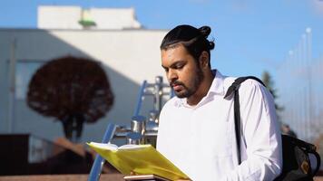 contento indio masculino estudiante lee libros cerca el Universidad video
