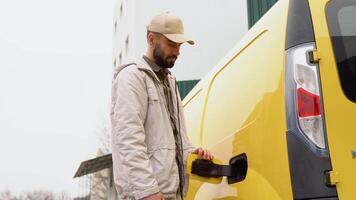 homem cobrando carga elétrico carro perto armazém. verde energia, eco amigáveis combustível video