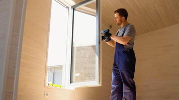 workman i overall montera PVC fönster med skruvmejsel i en ny trä- prefabricerad hus video