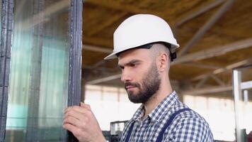 Professional man worker in uniform and helmet in a window warehouse prepares windows for sending video
