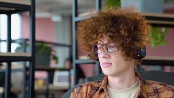 Jeune rouge -aux cheveux frisé étudiant pigiste écoute à la musique dans co travail espace tandis que séance sur confortable doux fauteuil video