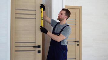 installazione di un' di legno interno porta. ritratto di giovane fabbro ferraio operaio nel uniforme installazione porta. professionale riparazione servizio. Manutenzione concetto video