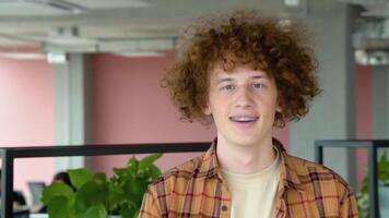 Happy redhead male freelancer with braces smiling at camera and walk in co working space video