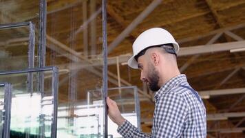 Professional man worker in uniform and helmet in a window warehouse prepares windows for sending video