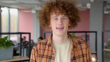 Happy redhead male freelancer with braces smiling at camera and walk in co working space video