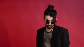 Portrait of a young gay man in sunglasses dressed in a mesh t-shirt on a red background video