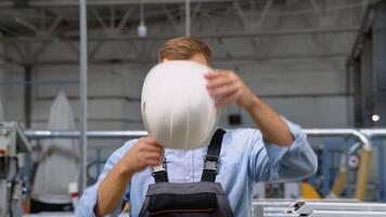 Portrait of the manual man worker in uniform puts on a helmet and looking to the camera video