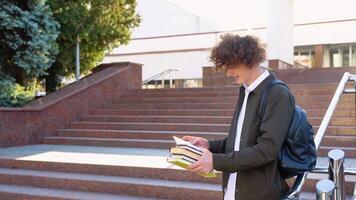 Young red -haired curly male student reads books near the university. Modern education, college tuition and grants, studentship and study abroad concept video