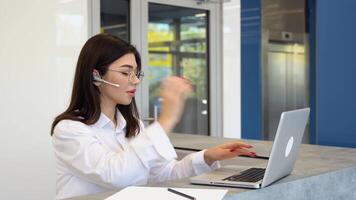 Female customer support operator with headset uses a laptop video