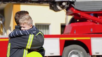 dapper brandweerman in uniform knuffels een weinig jongen met een speelgoed- tegen een brand motor video