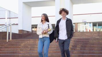 Two stylish students walk near the campus and smile. Friendly caucasian guy and girl walk together near the university video