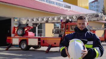 Portrait of the handsome fireman in the equipped costume taking off helmet and looking to the camera video