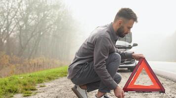 uomo mettendo triangolo attenzione cartello su nebbioso strada vicino rotto auto video