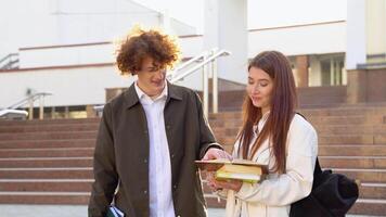 två studenter diskuterar nära de universitet. ung par, man och kvinna, talande på de campus bakgrund video