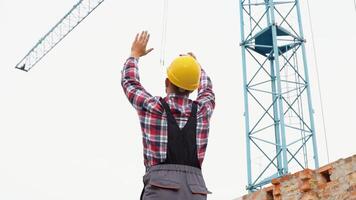 sérieux directeur dans casque et uniforme donnant commandes à grue opérateur. barbu homme faire des gestes et en criant pendant travail processus video