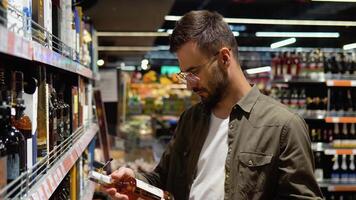 un joven hombre en un supermercado elige alcohol en el vino sección video