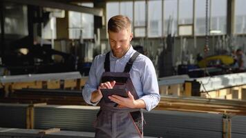 Professional heavy industry engineer worker wearing safety uniform uses tablet computer. Smiling caucasian industrial specialist standing in a metal construction manufacture video