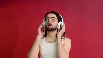 Jeune souriant content joyeux homme dans des lunettes et blanc T-shirt écoute à la musique sur rouge Couleur Contexte video