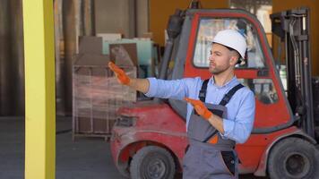 Serious manager in helmet and uniform giving commands to workers on industrial warehouse against the background of the warehouse loader. Bearded man gesturing and shouting during working process video