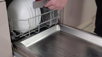 Young man loading dirty dishes into a dishwasher machine. A man uses modern appliance to keep the home clean. Close-up, top view video