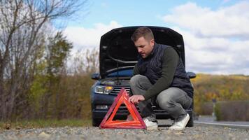 jong Mens zet het een rood driehoek naar waarschuwen andere weg gebruikers, auto afbreken of motor mislukking hou op Bij platteland straat video