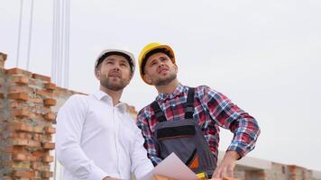 Two specialists inspect commercial, industrial building construction site. Real estate project with civil engineer. In the background crane, skyscraper concrete formwork frames. video