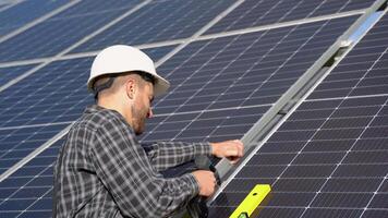 Male engineer in protective helmet installing solar photovoltaic panel system using screwdriver. Alternative energy ecological concept video