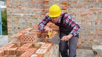 Installing brick wall. Construction worker in uniform and safety equipment have job on building video