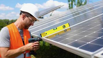 maschio ingegnere nel protettivo casco installazione solare fotovoltaico pannello sistema utilizzando Cacciavite. elettricista montaggio blu solare modulo su tetto di moderno Casa. alternativa energia ecologico concetto video