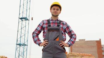 A construction worker in a yellow helmet looks forward at camera and smiles because of sustainability of industry. Concept of construction engineering works and real estate video