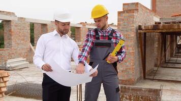Two construction workers look at an architectural drawing in house construction video