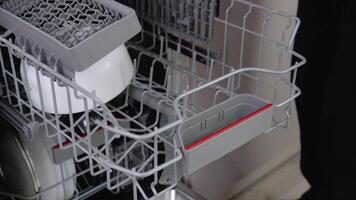 House chores concept.Housewife taking out clean plates from dishwasher machine. Female hands unloading dishwasher close up. Modern technologies for home video