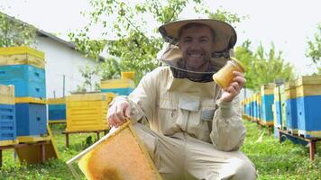 Closeup portrait of beekeeper holding a honeycomb frame and jar with honey. Beekeeping concept. Beekeeper harvesting honey video