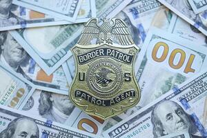 KYIV, UKRAINE - MARCH 9, 2024 US Border Patrol Agent badge on many US hundred dollar bills photo