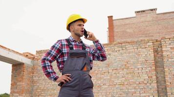 Construction worker in uniform and safety equipment have job on building. Talking by phone video