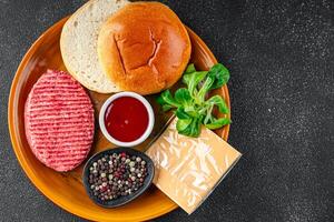 crudo hamburguesa conjunto chuleta, bollo, queso, tomate salsa, verduras Fresco Cocinando comida comida bocadillo en el mesa Copiar espacio comida antecedentes foto