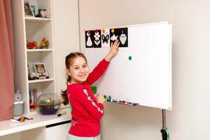 little girl plays school at home hanging pictures on the board photo