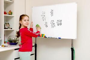 espalda a escuela, niña aprendizaje a resolver ejemplos en un columna en el tablero foto