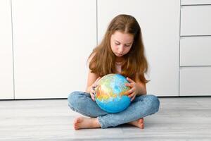 a little cute girl sitting on the floor carefully examines the globe photo