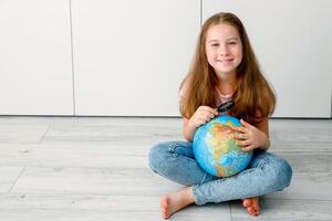 smiling little girl sitting on the floor with a globe and a magnifying glass photo