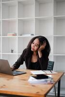 Businesswoman appears stressed as she leans on her hand, looking at her laptop in a modern office environment. photo